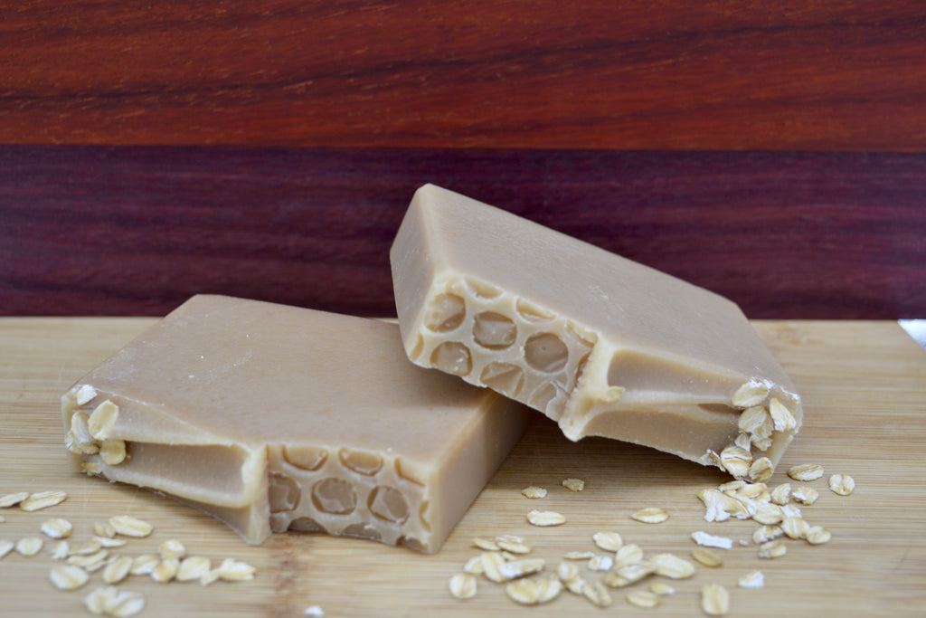 Two pieces of base soap with honey comb texture on top on a wooden surface with loose oats.