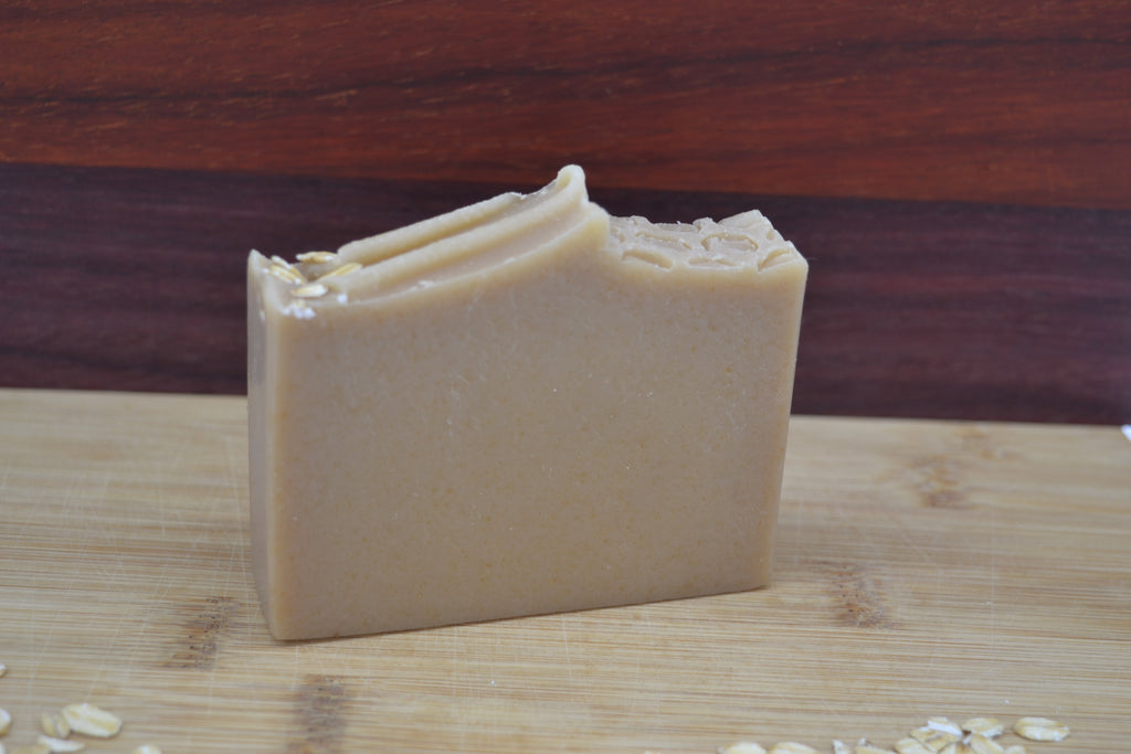 Beige Bar of soap with visible honeycomb texture and oat pieces on a wooden surface