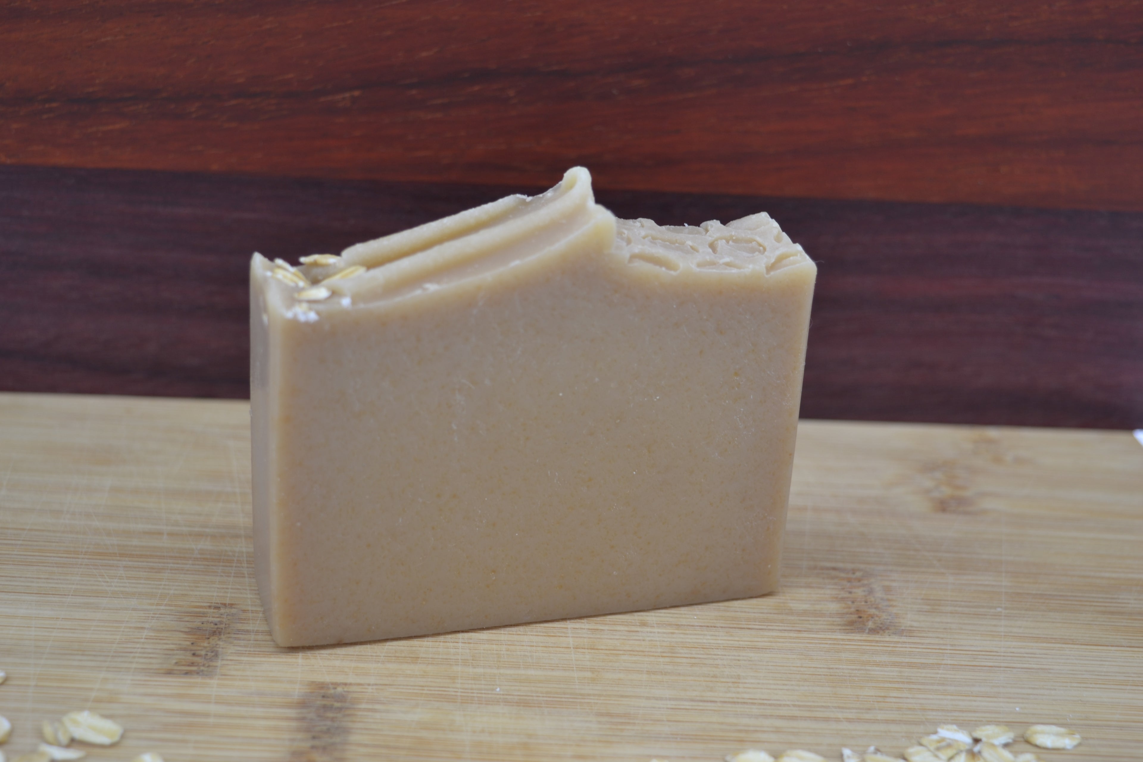 Beige Bar of soap with visible honeycomb texture and oat pieces on a wooden surface