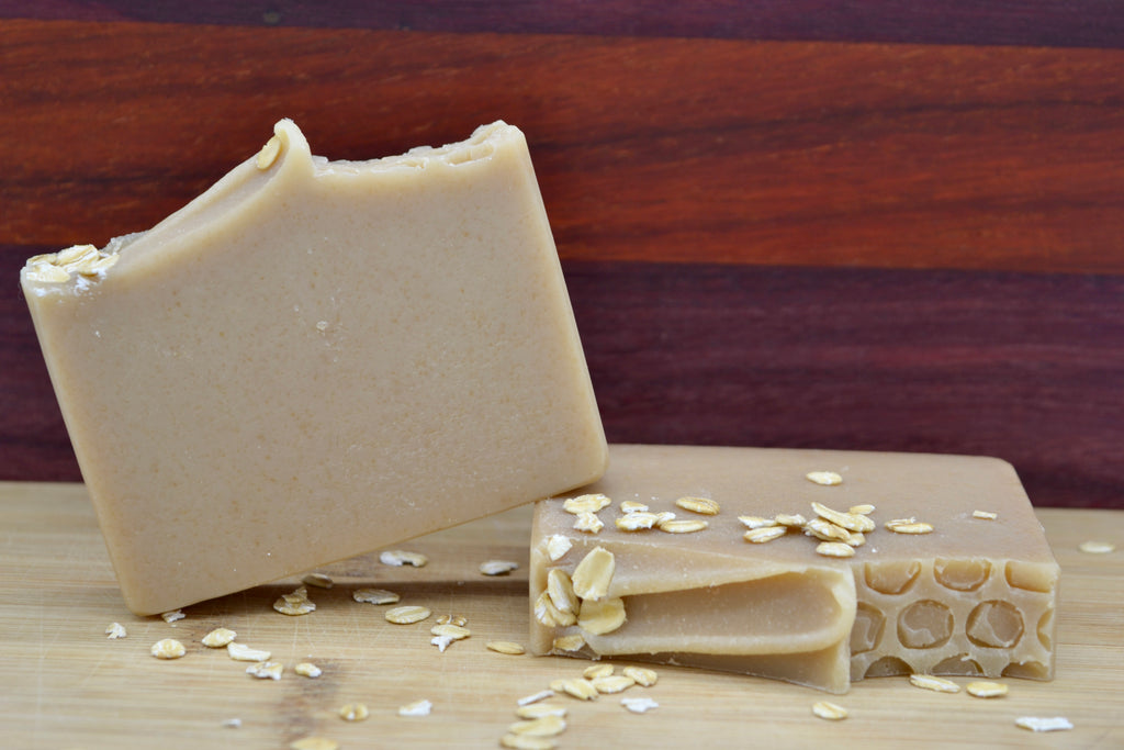 Two bars of beige soap with visible oatmeal pieces on a wooden surface.