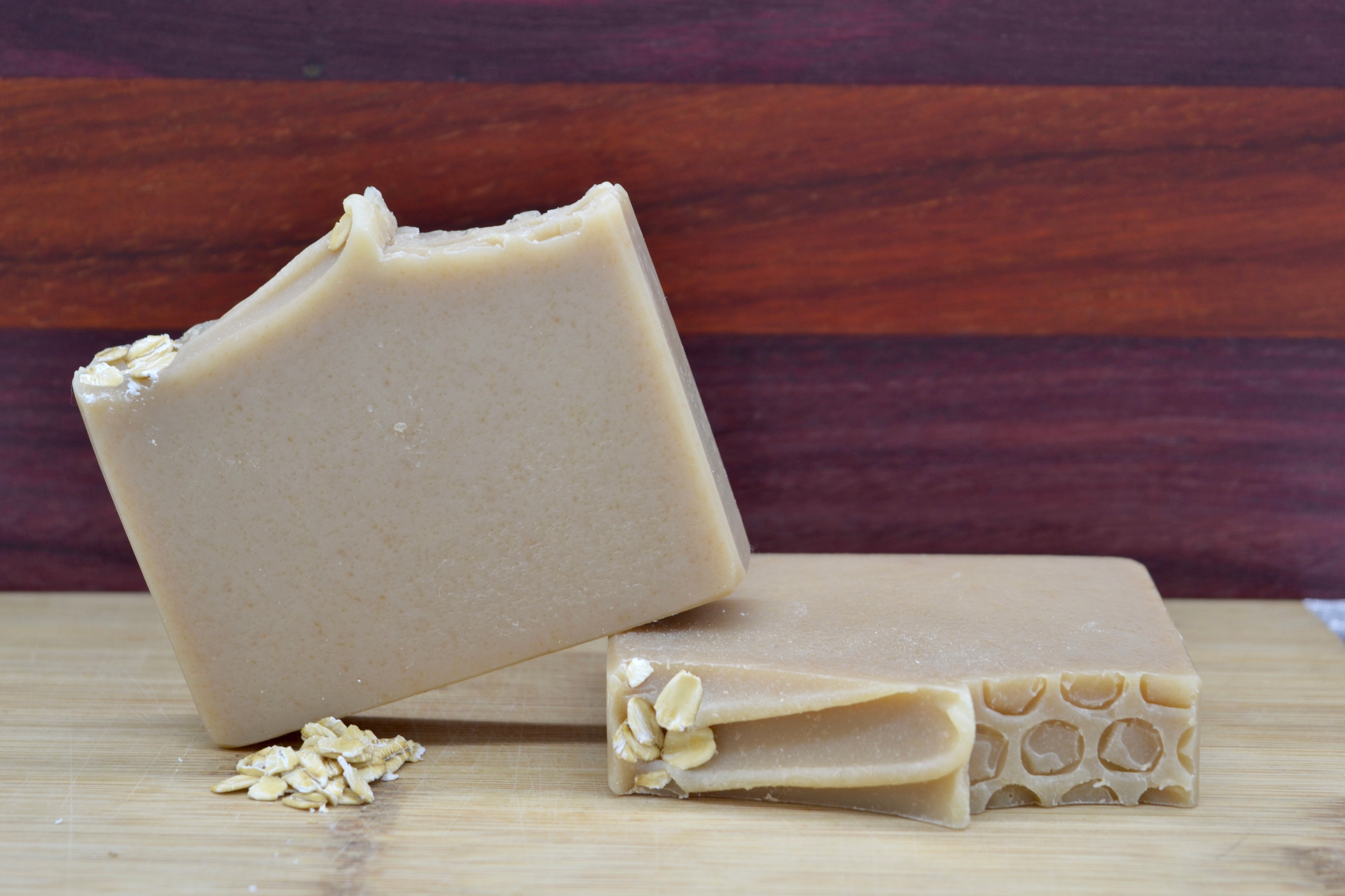 Two beige bars of soap with honeycomb and oatmeal on a wooden surface
