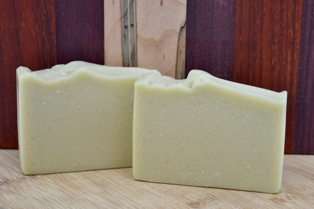 Two bars of light green soap on a wooden surface with a wooden background