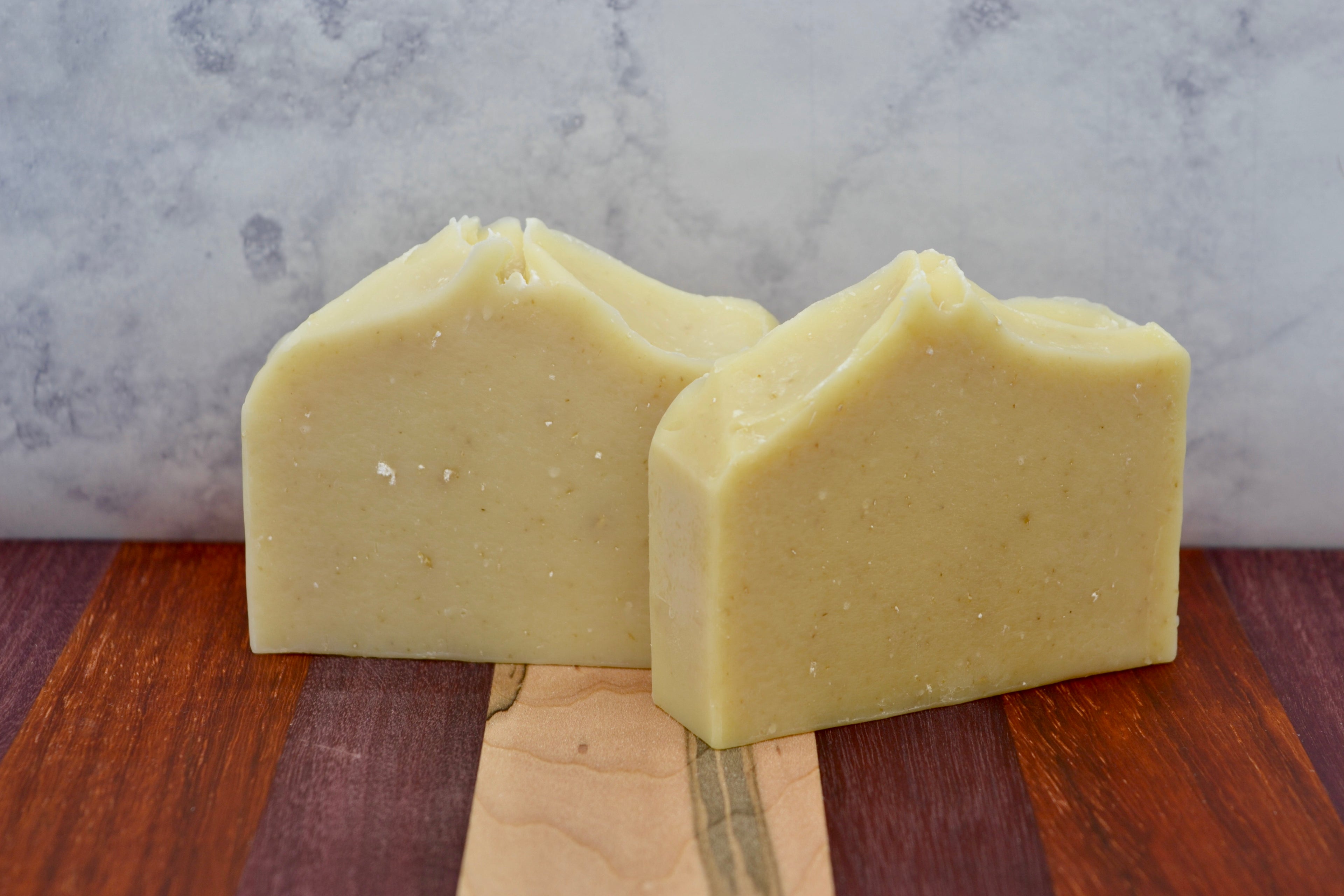 Two bars of cream soap on a wooden surface with a marble background