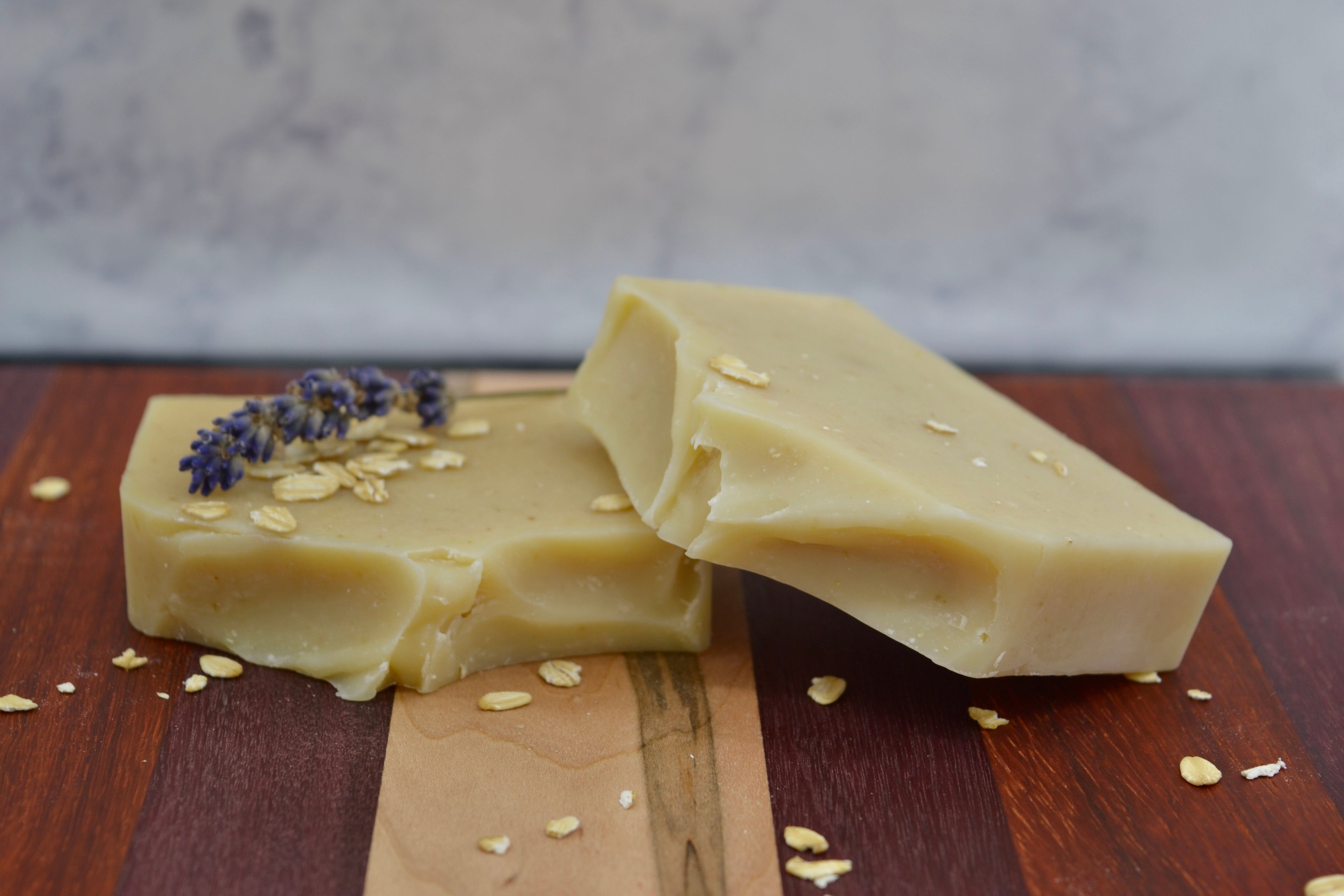 Two light cream bars of soap with lavender and oats on a wooden surface