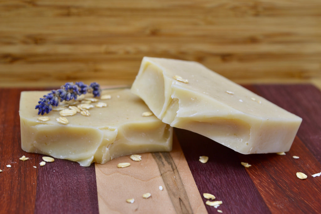 Two light cream bars of soap with lavender and oats on a wooden surface