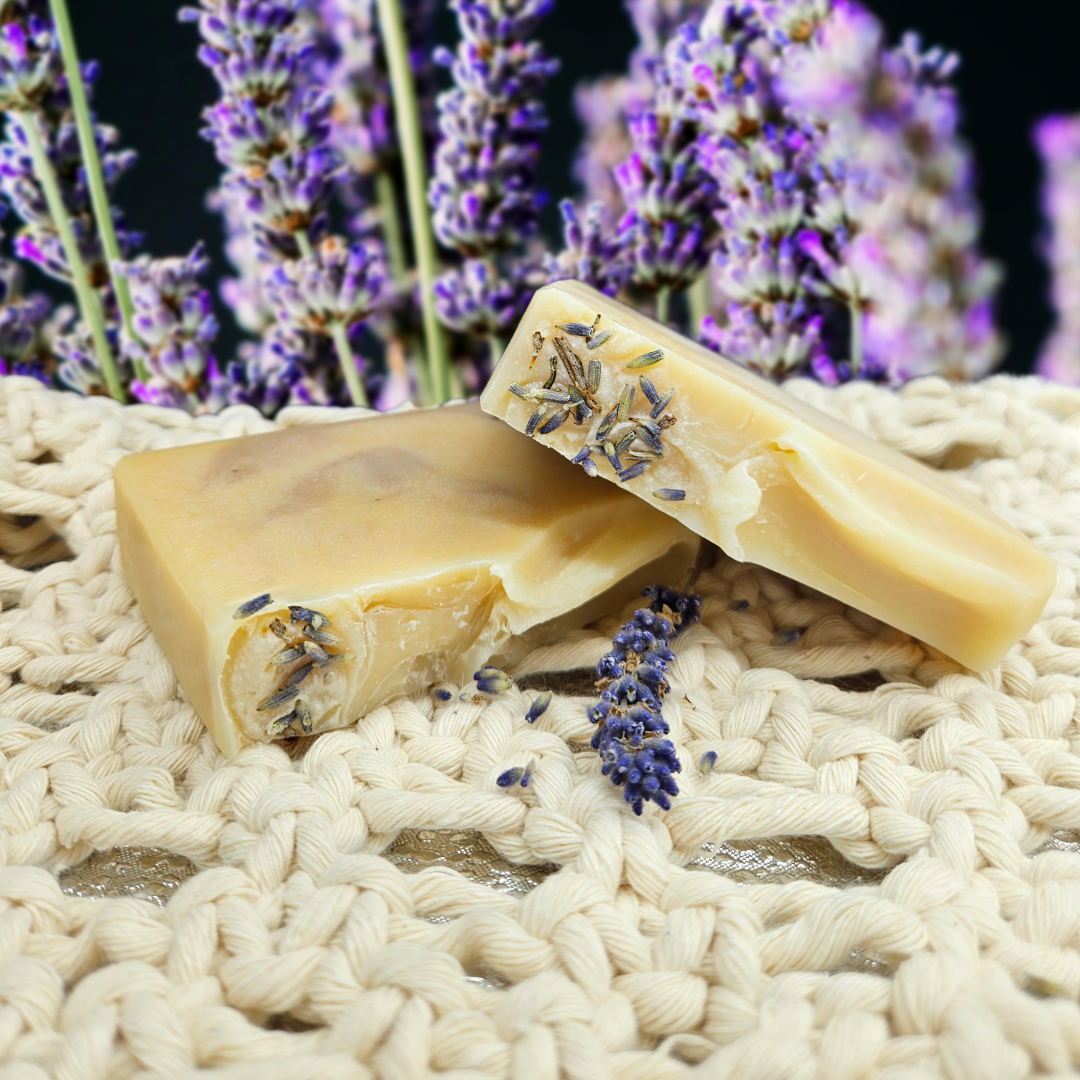 Two bars of soap with lavender on a woven surface, with lavender flowers in the background.