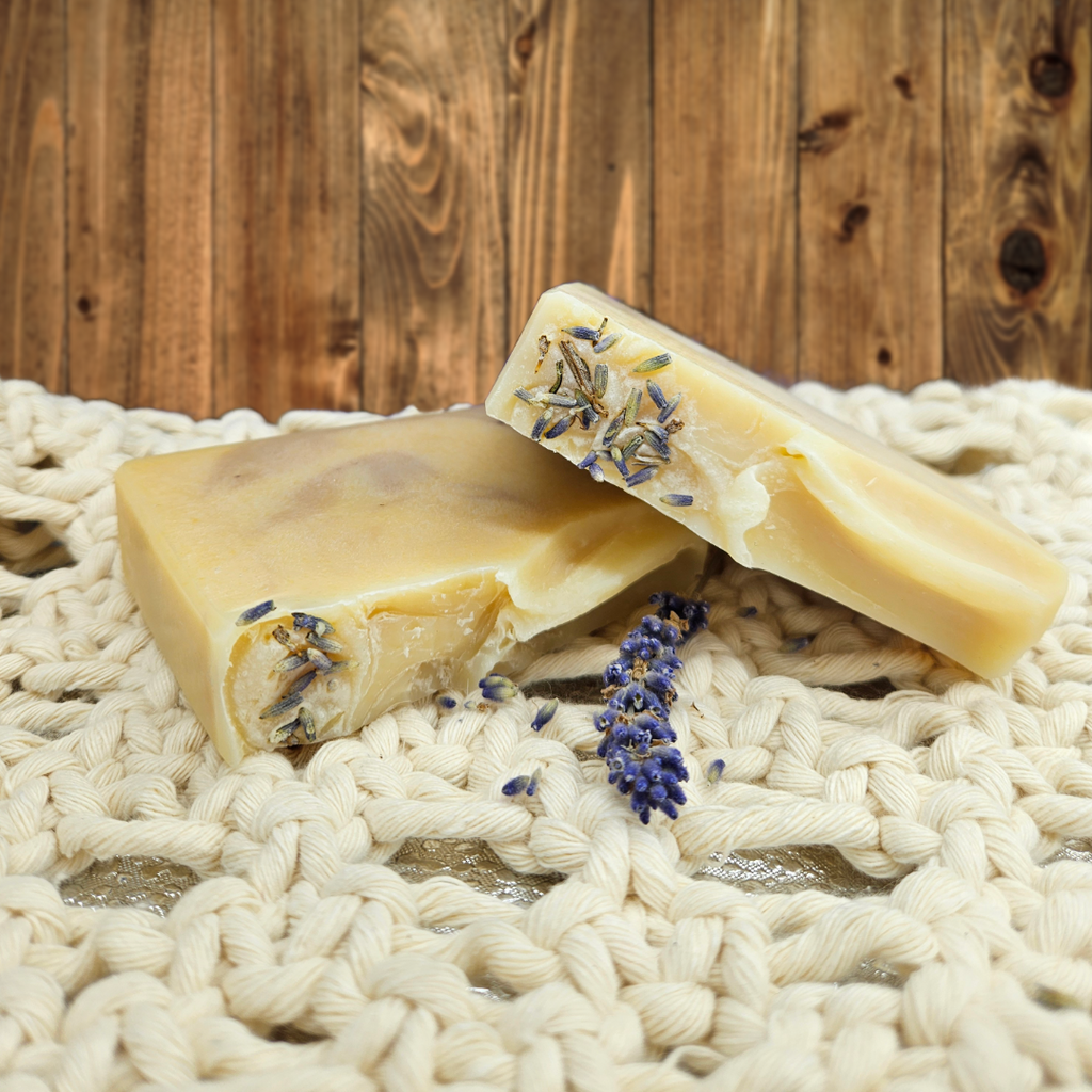 Two bars of soap with lavender on a woven surface and wooden background